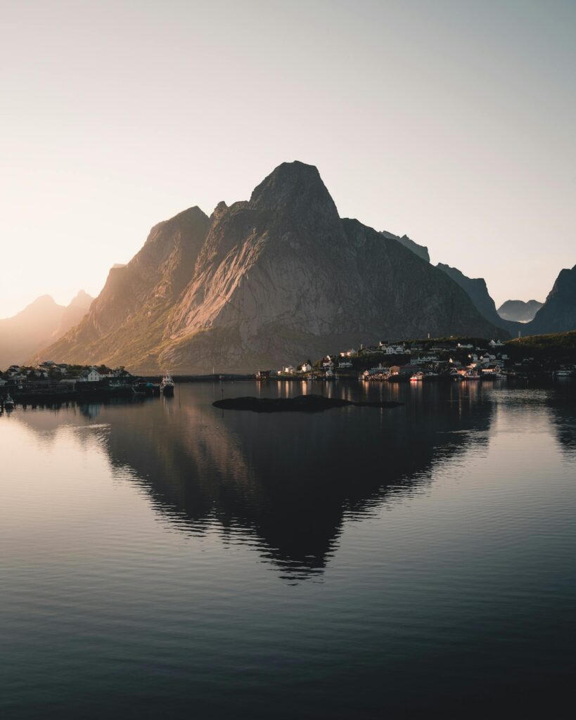 Nordic mountain landscape at sunrise with a calm coastal village and mountain reflection on still water.